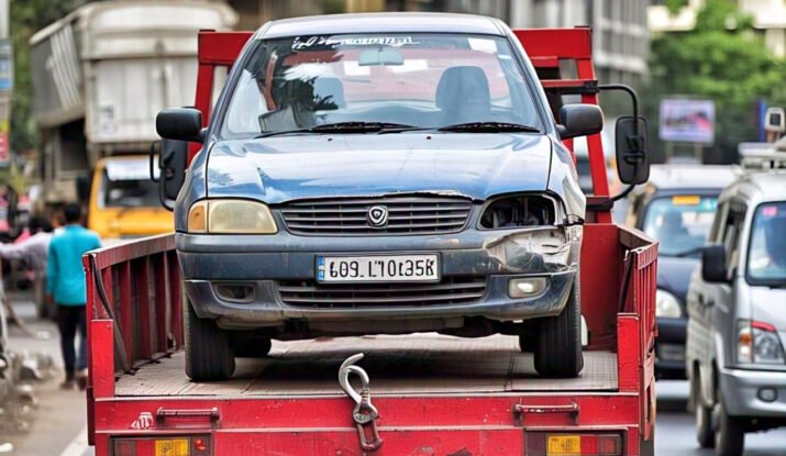 A damaged blue car being transported on a red tow truck in a busy street of Indore. Reliable towing services in Indore ensure fast and professional roadside assistance for vehicle breakdowns and accidents.